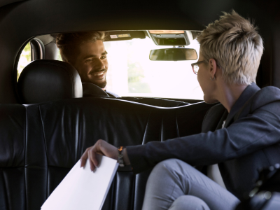 A man sitting in the back seat of a car talking to another man