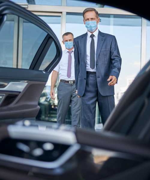 Two men in suits and masks standing in front of a car